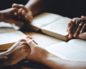 Christian group of people holding hands praying worship to believe and Bible on a wooden table for devotional or prayer meeting concept.